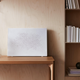 The white Symfonisk wall art speaker leaned against a wall on top of a table.